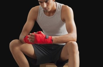 Thoughtful male boxer sitting against black background