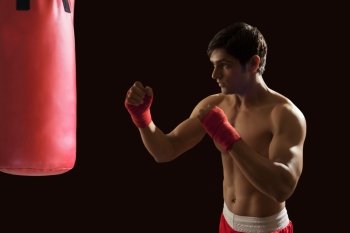 Young male boxer hitting red punching bag isolated over black background