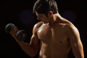 Young man exercising with dumbbell against black background