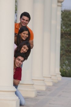 Portrait of smiling friends peeking from behind column outdoors