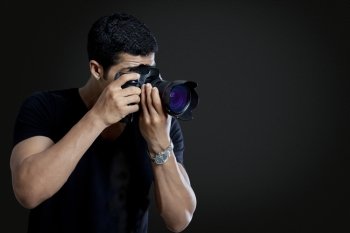 Male photographer taking photograph against black background 