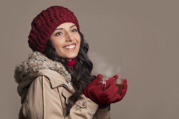 Young woman in warm clothes holding tea cup and looking away 