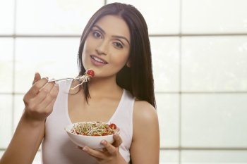 Young woman eating bean sprouts and cherry tomatoes against glass window 