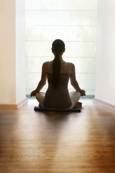 Rear view of young woman meditating on hardwood floor