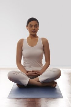 Young woman sitting in lotus position on mat