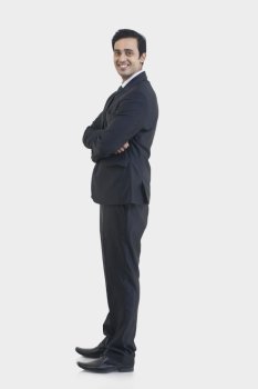 Side view of young businessman in suit standing against gray background 