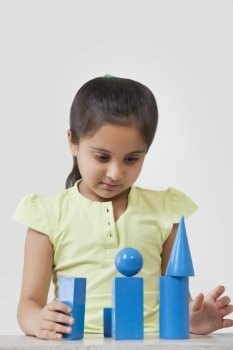 Little girl stacking geometry shaped blocks isolated over gray background 