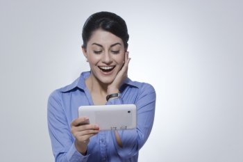 Delighted young businesswoman using digital tablet against gray background