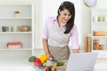 Smiling businesswoman using laptop while preparing food in kitchen