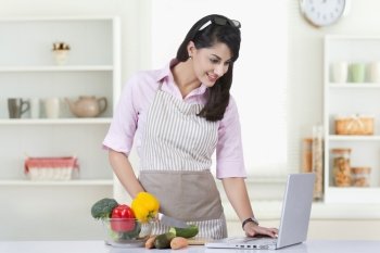 Businesswoman using laptop while preparing food in kitchen at home