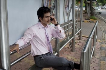 Businessman talking on a mobile phone at a bus stop 