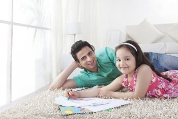 Portrait of father and daughter drawing while lying on rug at home