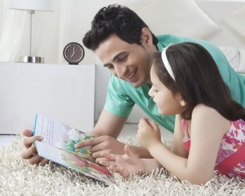 Happy father and daughter reading story book while lying on rug at home