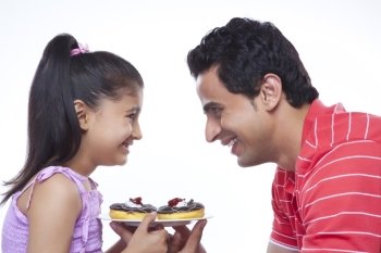 Side view of happy daughter and father holding plate of donuts against white background