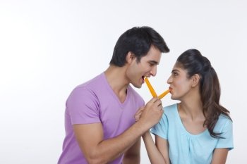 Romantic young couple feeding each other ice lollies over white background