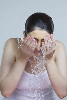 Young woman washing face with water over blue background