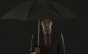 Portrait of confident businessman holding umbrella against black background