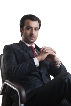 Portrait of confident young businessman sitting on chair against white background