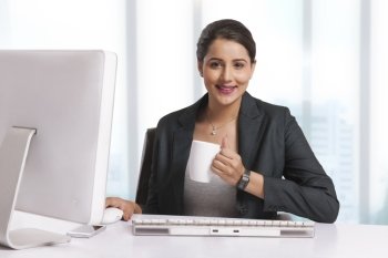Portrait of smiling businesswoman having coffee at desk in office