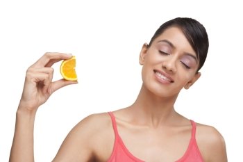 Close-up of smiling woman squeezing slice of orange with eyes closed 