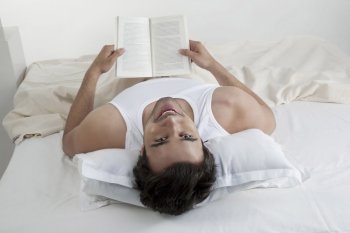 Man holding a book while lying in bed 