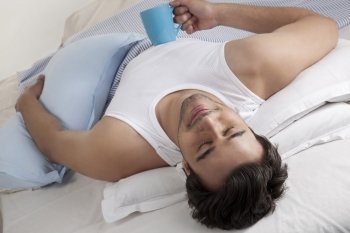 Man lying in bed with a cup of coffee 