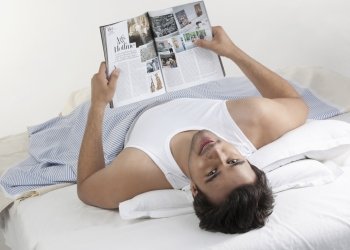 Man holding a magazine while lying in bed 