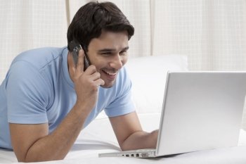 Man talking on the phone while working on a laptop 
