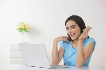 Portrait of happy young woman with credit card and laptop at home