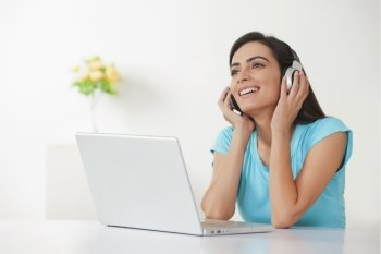 Happy young woman listening music through headphones with laptop at table