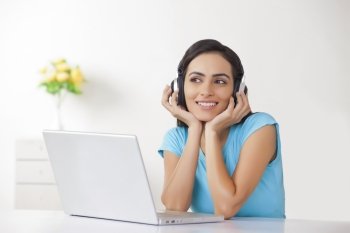 Beautiful woman listening to headphones in front of laptop at home