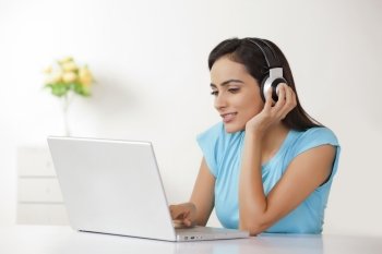 Young woman listening to headphones while using laptop at home