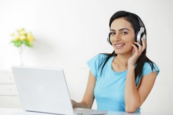Portrait of beautiful young woman with laptop listening to headphones at home