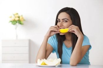 Portrait of beautiful young woman eating slice of melon at home