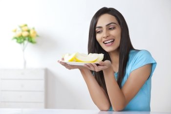 Young woman holding plate with slices of melon at home