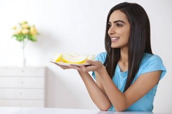 Beautiful young woman holding plate with slices of melon at home