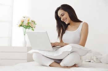 Beautiful young woman in nightwear using laptop on bed