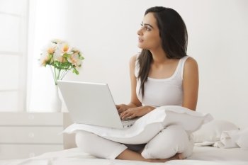 Thoughtful young Indian woman using laptop on bed