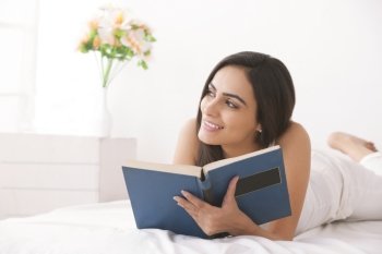 Thoughtful young woman reading book in bed