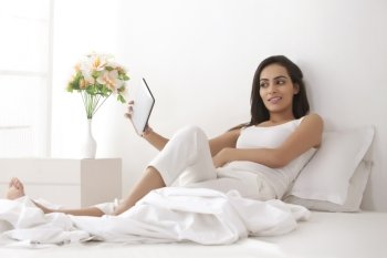 Full length of beautiful young woman taking self-portrait through digital tablet in bed