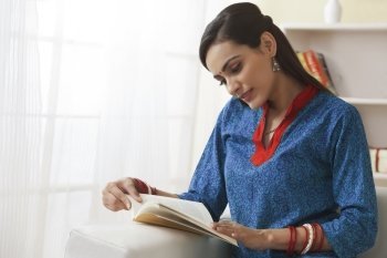 Young Indian woman reading book on sofa