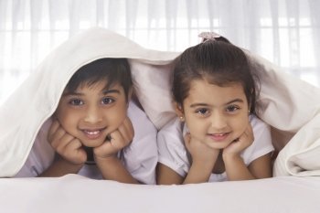 Portrait of cute siblings under blanket in bed