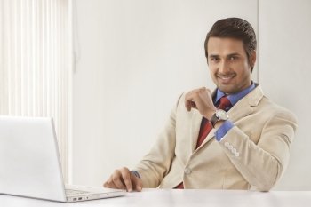 Portrait of handsome young businessman with laptop at office desk