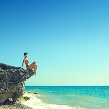 Elegant young woman sits on rocky shore 