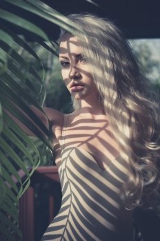 Beautiful blonde and the sun’s rays through the palm leaf
