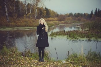 Beautiful elegant woman in a black coat on the river bank