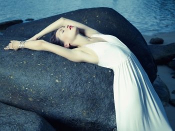 Beautiful elegant lady with a huge boulder on the seashore