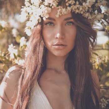 Portrait of beautiful romantic lady in a wreath of apple trees in the summer garden
