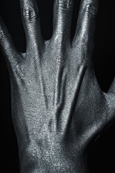 Man’s hand in silver paint on black background closeup