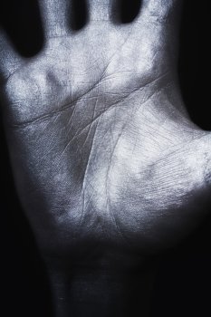 Man’s hand in silver paint on  black background closeup